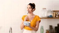Vrouw zit op aanrecht yoghurt te eten