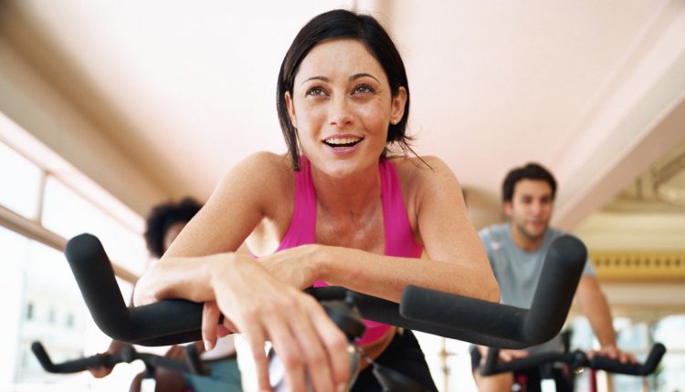 Vrouw in de sportschool op een spinningfiets, met waterfles in de hand