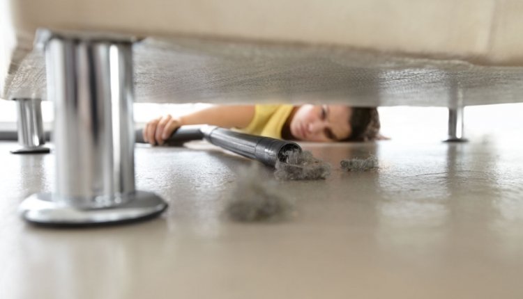 Vrouw ligt op de grond om onder bed te stofzuigen