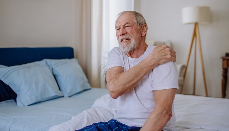 Man met zere schouders zittend op een bed