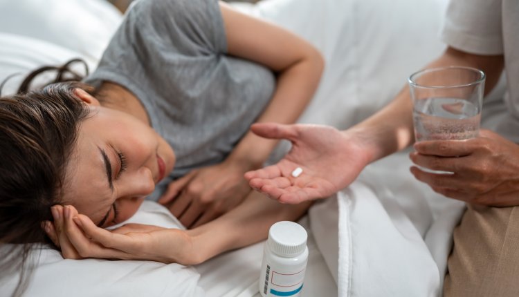 Vrouw met klachten op bed neemt medicatie