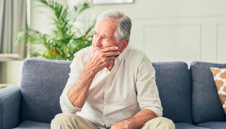 Man zit in zijn woonkamer op de bank, kijkt zorgelijk