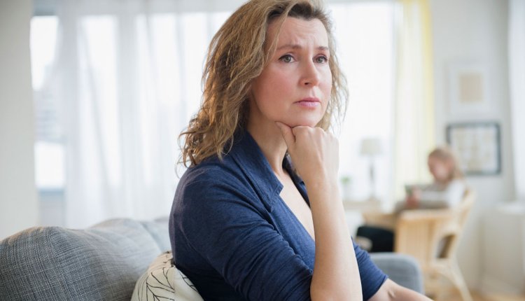 Vrouw kijkt zorgelijk zittend op de bank in haar woonkamer