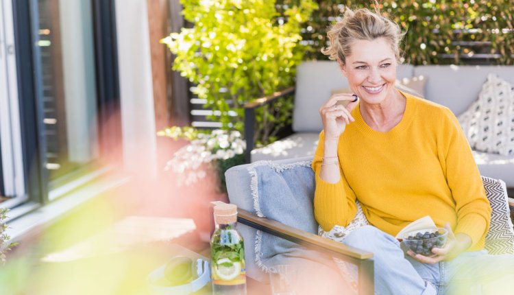 Vrouw zit op terras en eet blauwe bessen