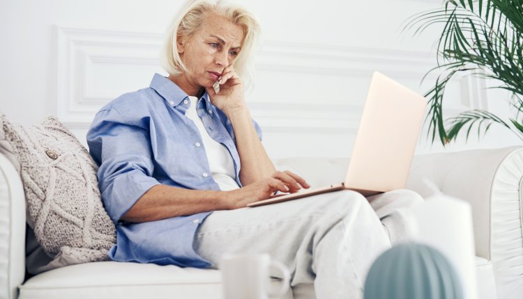 Vrouw zit met laptop op schoot op de bank