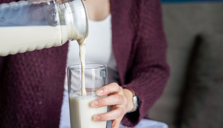 Vrouw schenkt havermelk in een groot glas