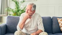 Man zit in zijn woonkamer op de bank, kijkt zorgelijk