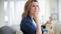 Vrouw kijkt zorgelijk zittend op de bank in haar woonkamer