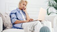 Vrouw zit met laptop op schoot op de bank