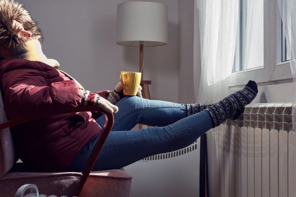 Vrouw met jas aan en muts op bij de verwarming