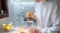 Vrouw perst citroen uit boven glas water