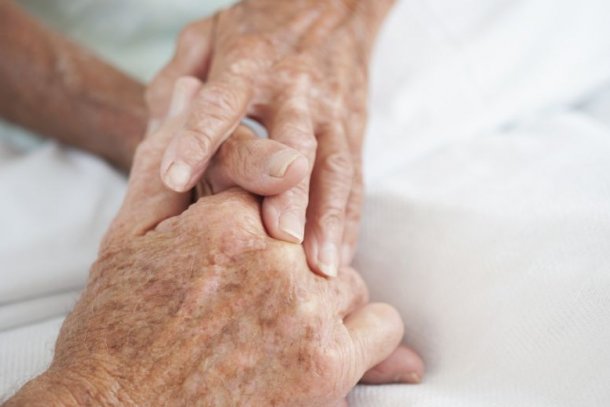 Twee handen van een ouder persoon houden een andere hand vast