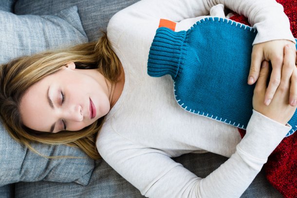 Vrouw ligt op bank met warmwaterkruik op haar buik