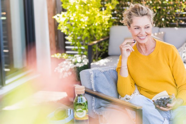 Vrouw zit op terras en eet blauwe bessen