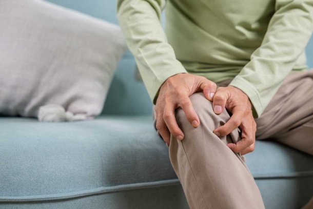 man net pijnlijke knie op de bank